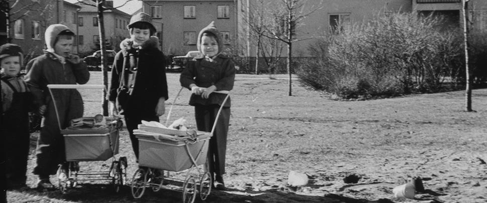 svartvitt foto av 4 barn med 3 dockvagnar framför hyreshus på Wetterlinsgatan. Bilden tagen på 1950-talet. 