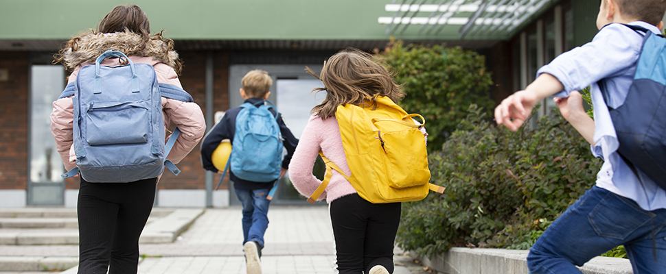 Skolbarn med ryggsäckar i olika färger springer mot skolans entré.