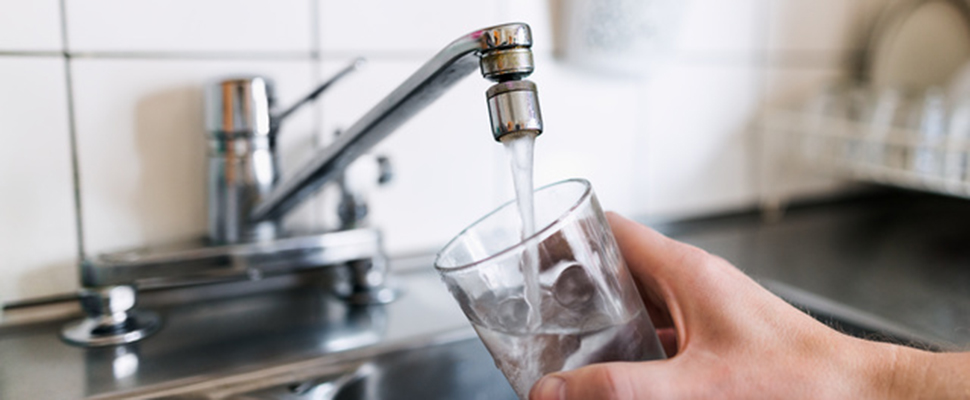 En person fyller på vatten i ett glas under en kran i köket.